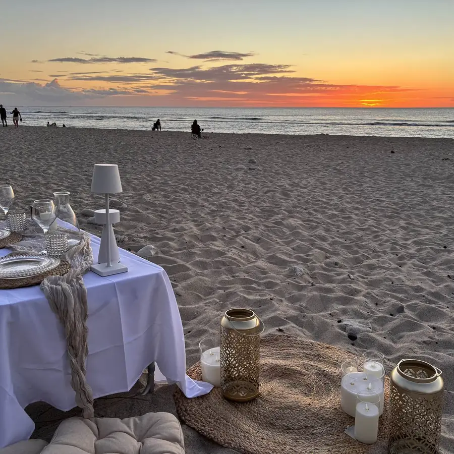 Table dressée pour un pique-nique romantique sur la plage au coucher du soleil